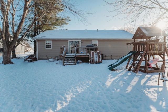 snow covered house with a playground and a wooden deck