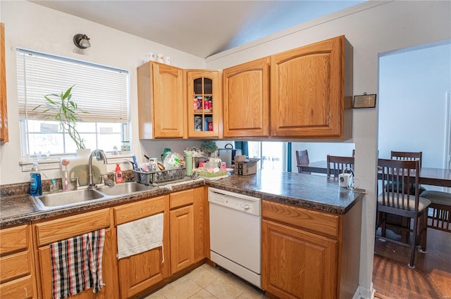 kitchen with white dishwasher, a sink, dark countertops, lofted ceiling, and glass insert cabinets