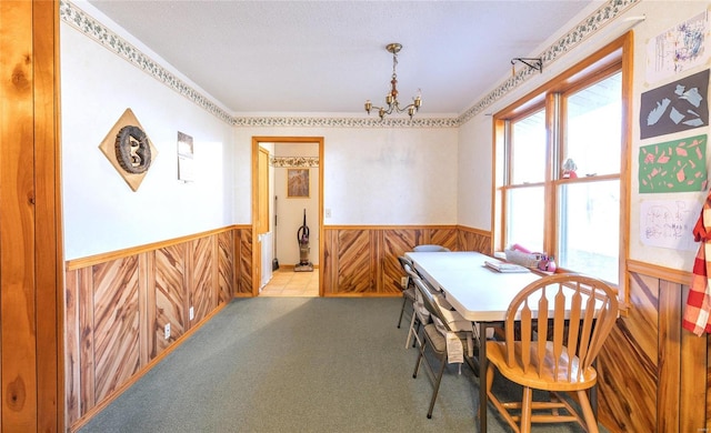 dining room with wainscoting, a chandelier, carpet floors, and wood walls