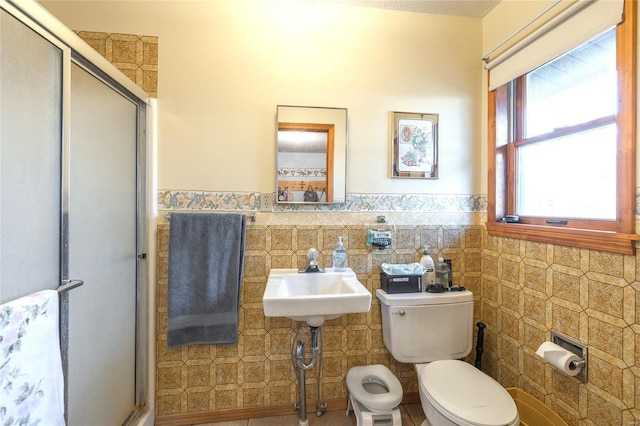 full bath featuring tile walls, toilet, a stall shower, wainscoting, and a sink