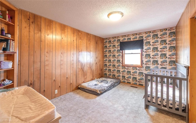 carpeted bedroom with a textured ceiling, wallpapered walls, and wooden walls