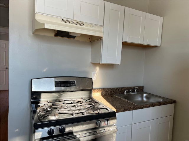 6514 Julian Ave, Saint Louis, MO 63133 - kitchen featuring stainless steel range with gas stovetop, under cabinet range hood, a sink, dark countertops, and white cabinetry