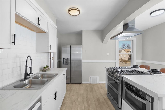 1100 Northdale Ave, Saint Louis, MO 63138 - kitchen featuring stainless steel appliances, a sink, wall chimney range hood, tasteful backsplash, and light wood finished floors