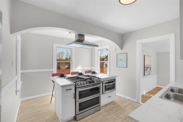 1100 Northdale Ave, Saint Louis, MO 63138 - kitchen with arched walkways, wall chimney exhaust hood, stainless steel appliances, and light wood-style flooring