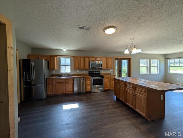 kitchen with appliances with stainless steel finishes, a sink, butcher block counters, a chandelier, and dark wood-style floors