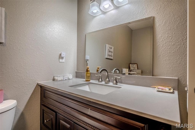 half bath featuring a textured wall, vanity, and toilet