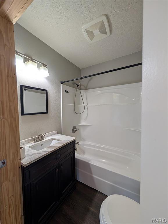 full bath featuring wood finished floors, a textured ceiling, toilet, shower / bath combination, and vanity
