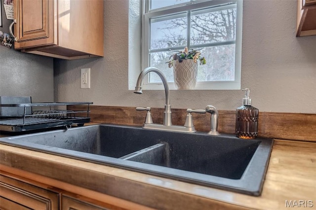 kitchen view of a sink, a textured wall, and brown cabinetry