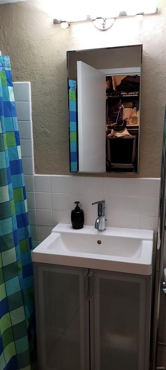 full bathroom with tile walls, vanity, a textured wall, a wainscoted wall, and curtained shower