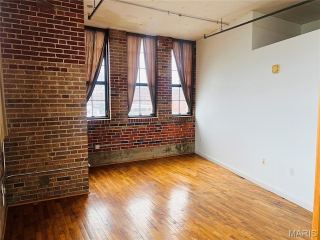 2020 Washington Ave Unit 504, Saint Louis, MO 63103 - unfurnished room featuring wood-type flooring, brick wall, baseboards, and rail lighting