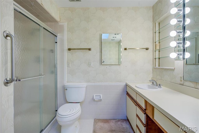 bathroom with wallpapered walls, toilet, a shower stall, vanity, and a wainscoted wall