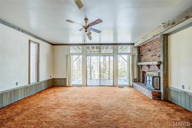 unfurnished living room featuring carpet flooring, healthy amount of natural light, ceiling fan, a wainscoted wall, and wood walls