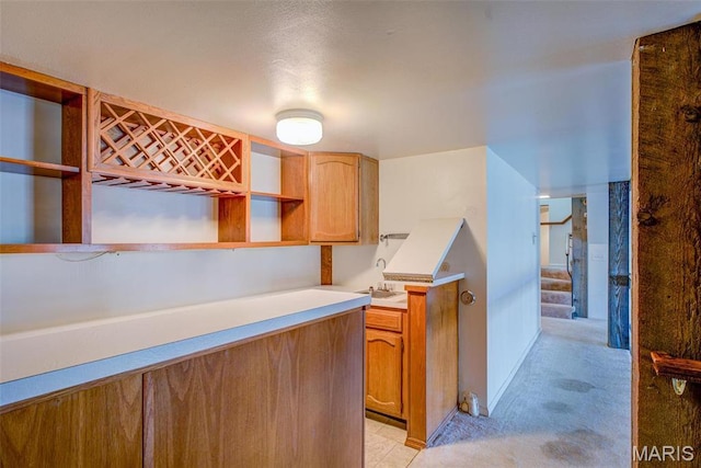 kitchen with open shelves, light colored carpet, light countertops, and brown cabinets