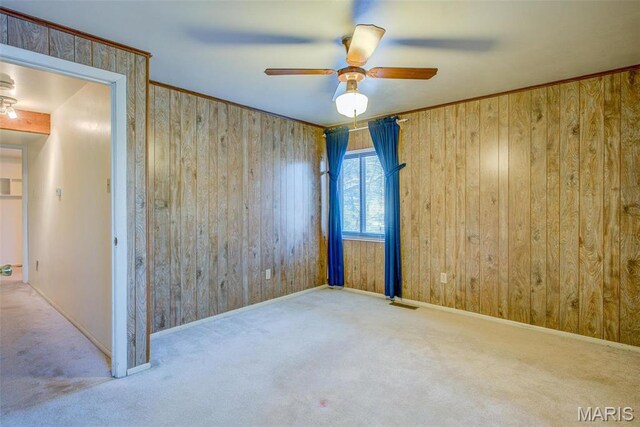 unfurnished room featuring carpet floors, wooden walls, ceiling fan, and baseboards
