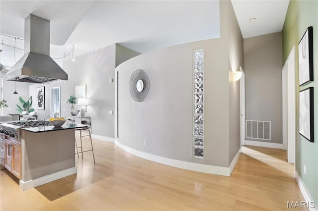 kitchen with island range hood, stainless steel gas stovetop, light wood-type flooring, baseboards, and a breakfast bar