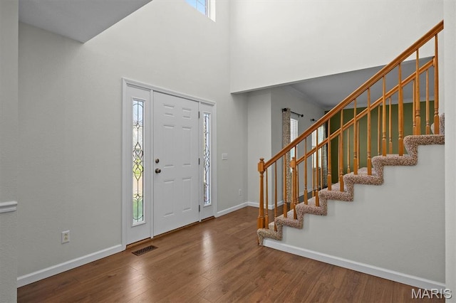 foyer featuring wood finished floors, stairs, baseboards, and a towering ceiling