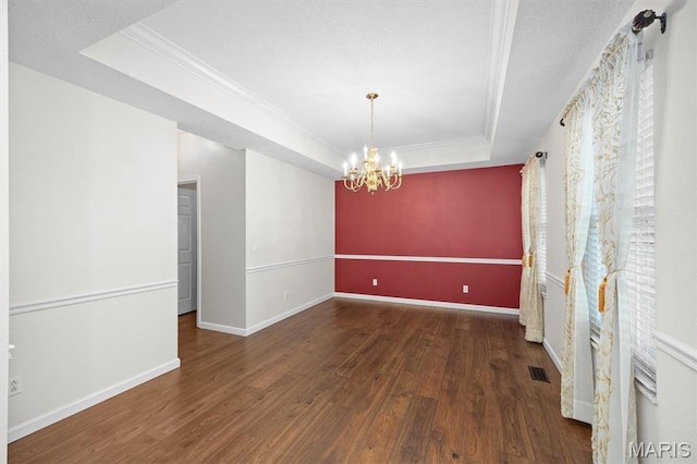 unfurnished room with a raised ceiling, ornamental molding, wood finished floors, a chandelier, and baseboards
