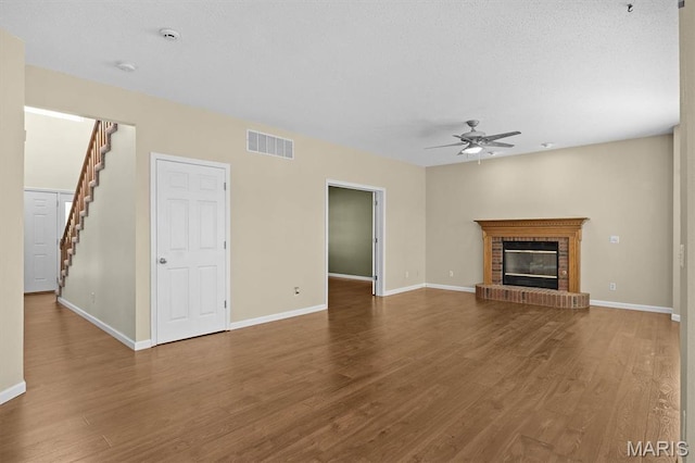 unfurnished living room with ceiling fan, stairway, wood finished floors, baseboards, and a fireplace