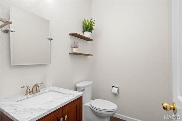 half bathroom with vanity, toilet, and baseboards