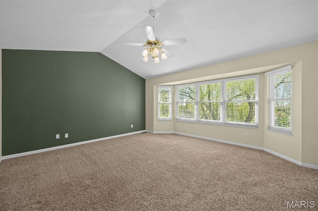carpeted empty room with a ceiling fan, vaulted ceiling, and baseboards