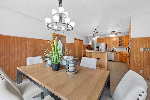 dining area with wooden walls, a chandelier, a wainscoted wall, a ceiling fan, and light tile patterned floors