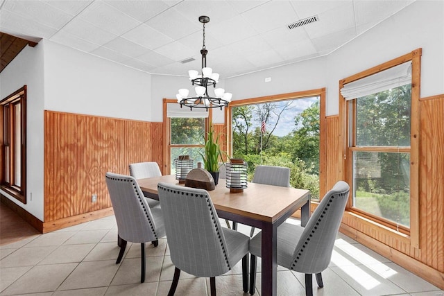 dining area featuring wood walls, a chandelier, wainscoting, and a drop ceiling