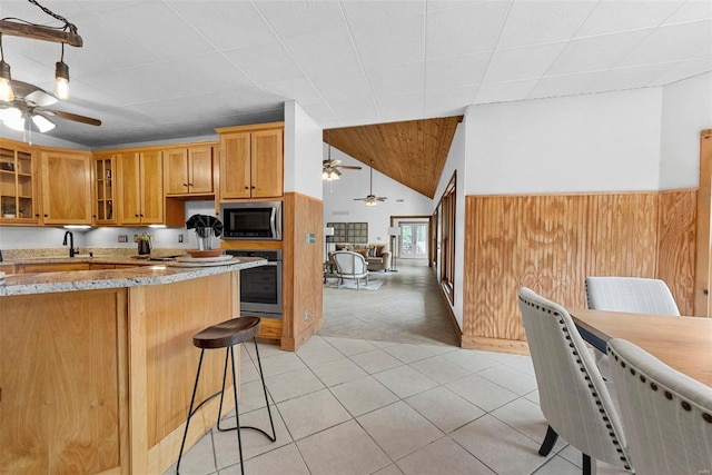 kitchen featuring stainless steel appliances, a ceiling fan, a sink, light stone countertops, and glass insert cabinets