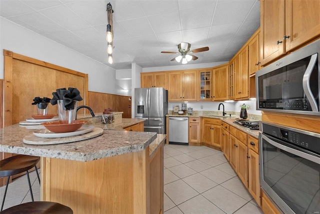 kitchen featuring appliances with stainless steel finishes, light tile patterned flooring, a sink, a breakfast bar, and ceiling fan