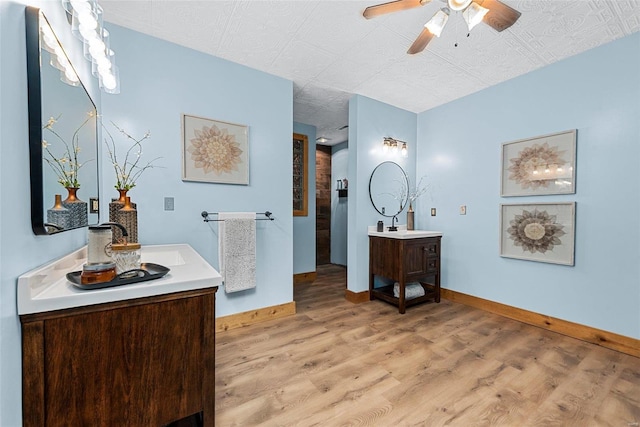 full bath with a ceiling fan, two vanities, wood finished floors, and baseboards