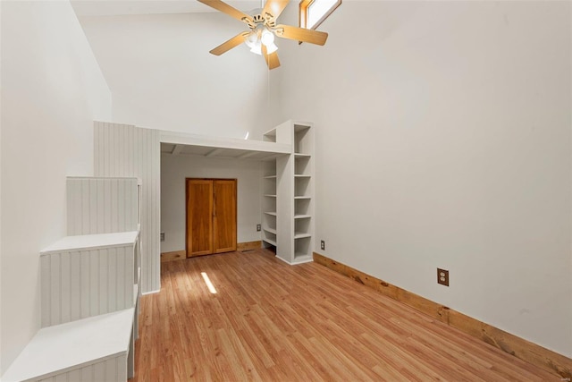 unfurnished living room featuring a high ceiling, light wood-style floors, a ceiling fan, and baseboards