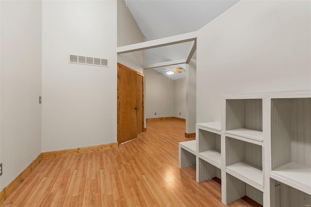 hallway featuring light wood finished floors, baseboards, and vaulted ceiling
