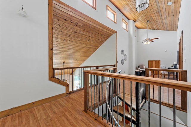 corridor with wood ceiling, wood finished floors, an upstairs landing, baseboards, and high vaulted ceiling