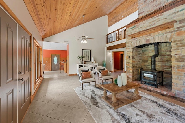 tiled living area featuring high vaulted ceiling, a wood stove, a ceiling fan, wood ceiling, and baseboards
