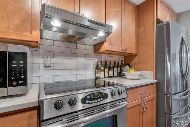 200 S Brentwood Unit 12F, Saint Louis, MO 63105 - kitchen with stainless steel appliances, under cabinet range hood, tasteful backsplash, light countertops, and brown cabinets