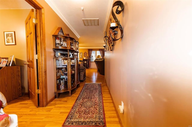 corridor with light wood-style floors, crown molding, and baseboards