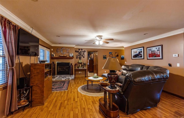 living room featuring wood finished floors, a ceiling fan, a fireplace, and crown molding
