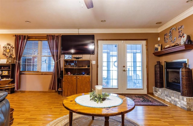 living area with light wood-style flooring, french doors, a brick fireplace, ornamental molding, and a ceiling fan