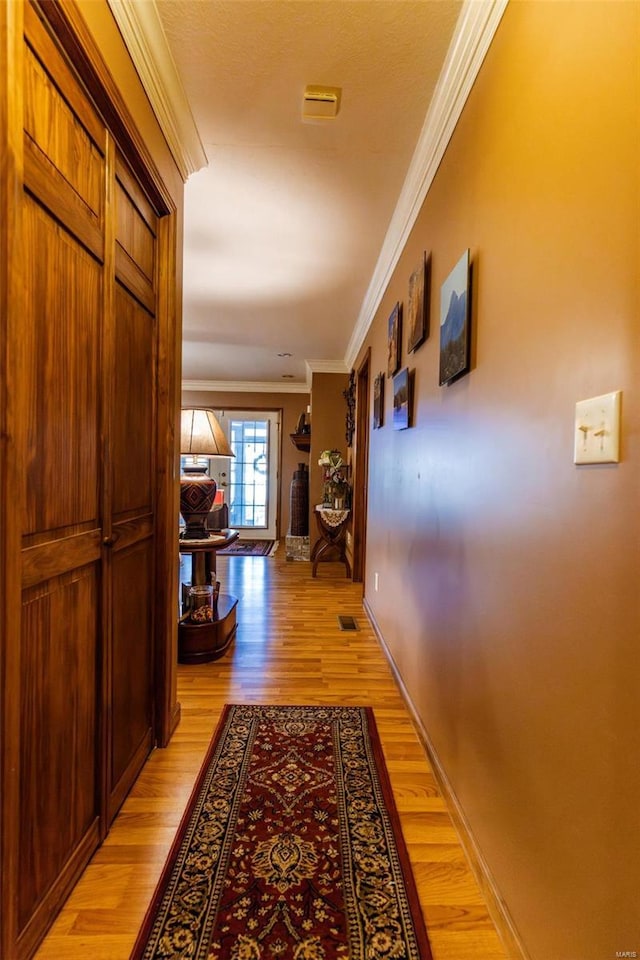 corridor featuring ornamental molding, light wood finished floors, and baseboards