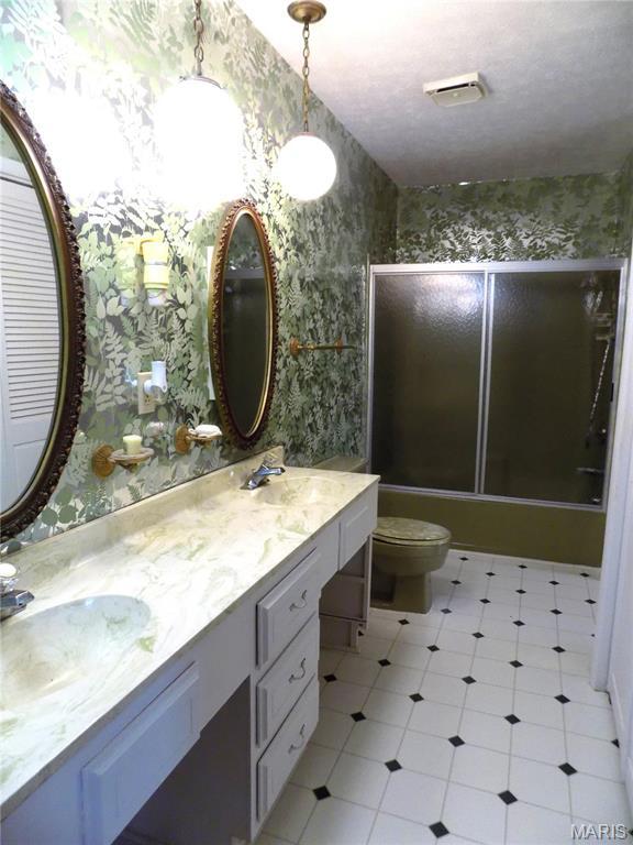 1306 Broadway St, Rolla, MO 65401 - bathroom featuring wallpapered walls, double vanity, bath / shower combo with glass door, and toilet