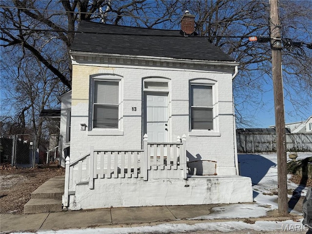 view of front facade featuring brick siding, a chimney, fence, and a shingled roof