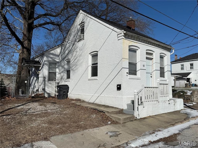view of home's exterior featuring a chimney, brick siding, and fence