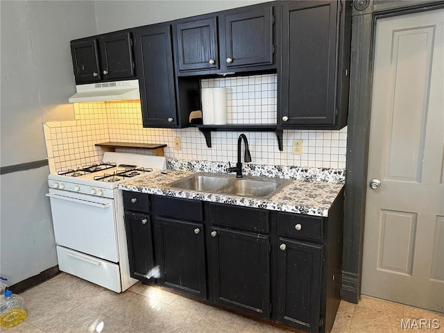 kitchen featuring white gas range oven, under cabinet range hood, a sink, dark cabinets, and decorative backsplash