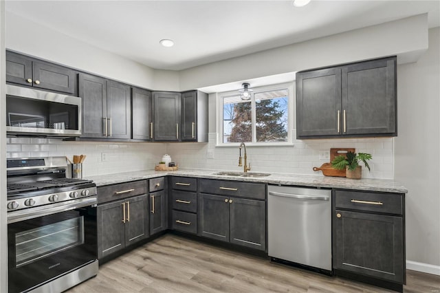11567 Joslyn Ct, Saint Louis, MO 63138 - kitchen with stainless steel appliances, a sink, light stone counters, light wood-style flooring, and decorative backsplash