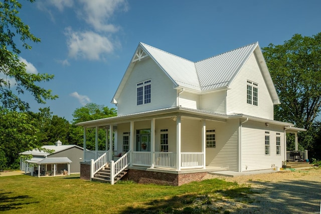 rear view of house with covered porch, a lawn, and metal roof