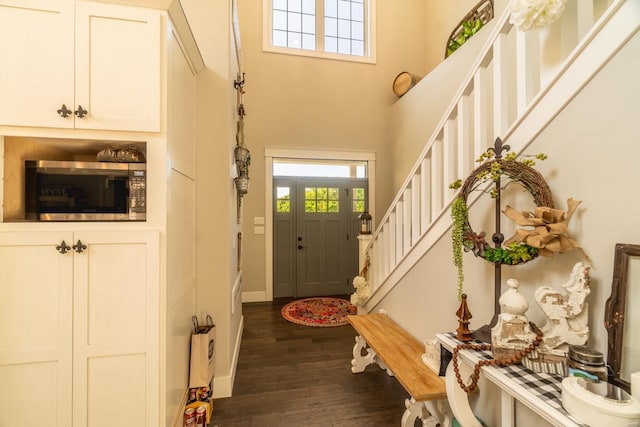 doorway featuring stairs, a towering ceiling, dark wood finished floors, and baseboards