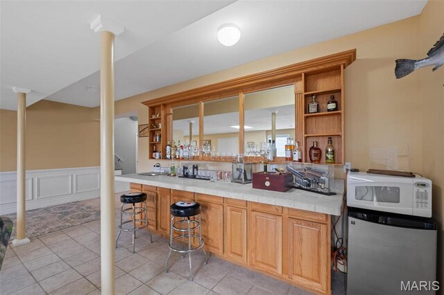 850 Aj Farm Ln, Washington, MO 63090 - indoor wet bar with white microwave, freestanding refrigerator, light tile patterned floors, a wainscoted wall, and stairway