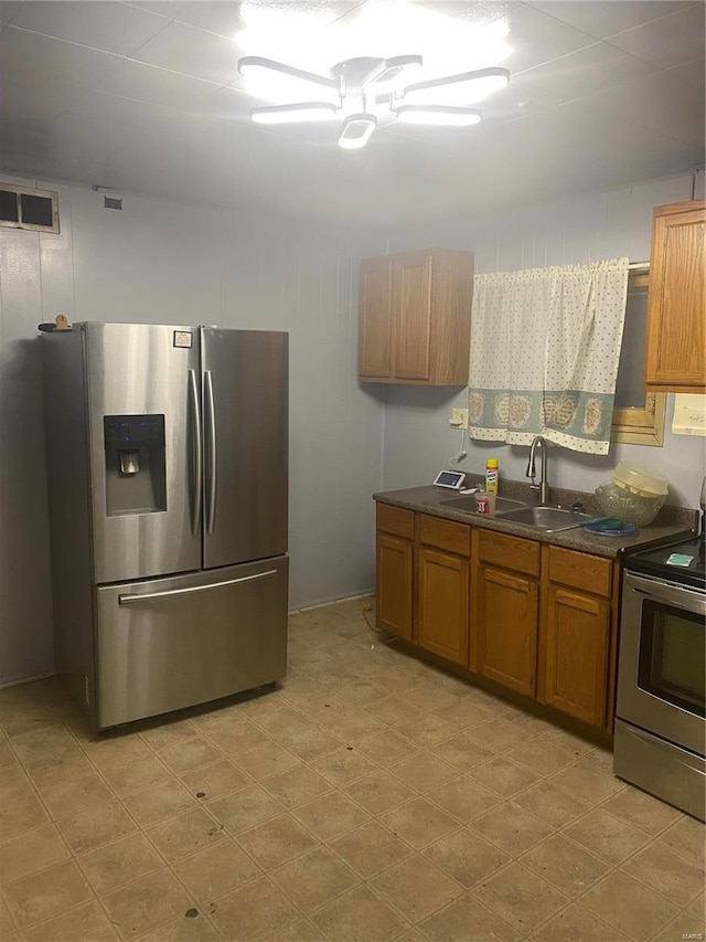 kitchen featuring stainless steel appliances, a sink, dark countertops, brown cabinets, and light flooring