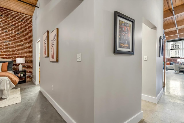 hallway featuring concrete flooring, baseboards, wooden ceiling, a towering ceiling, and beam ceiling