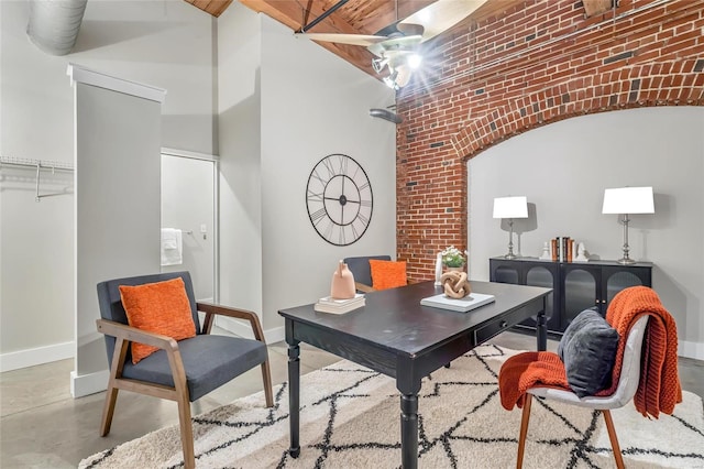 office space featuring baseboards, concrete flooring, brick wall, and a high ceiling