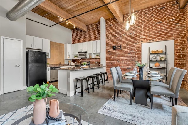 dining room with wood ceiling, finished concrete flooring, a high ceiling, brick wall, and beamed ceiling